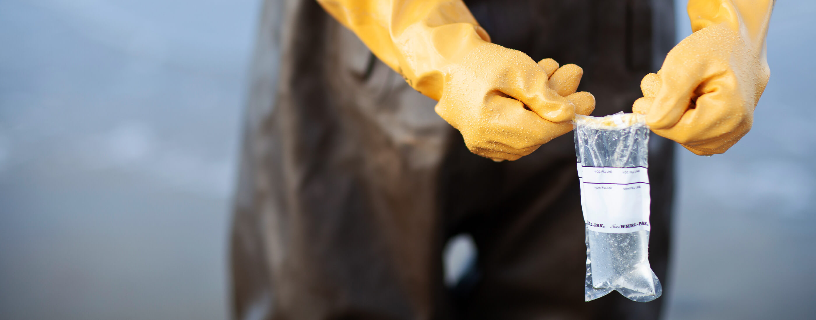 Hands in yellow gloves hold up water sample bag