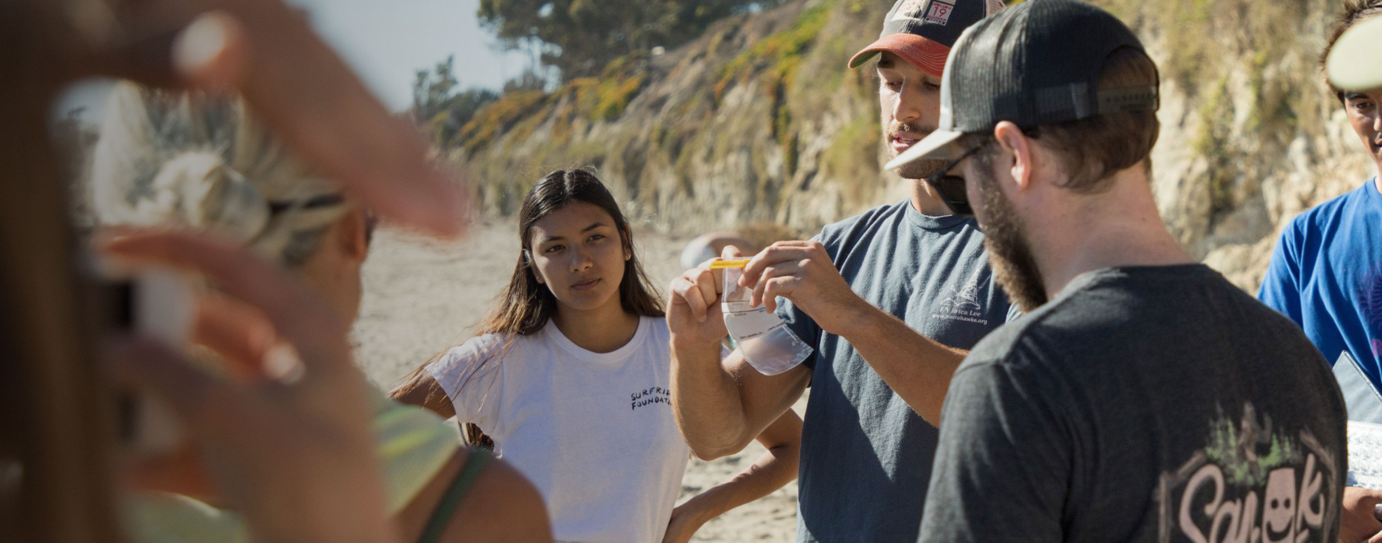 Man holds up plastic sample bag in front of group of people standing in a circle